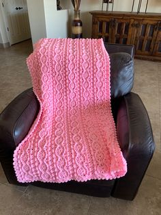 a pink crocheted blanket sitting on top of a leather chair