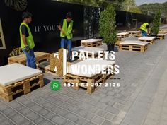 men in yellow vests are standing near wooden benches and tables with cushions on them