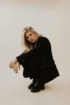 a woman is sitting on the floor in black boots and a coat, posing for a photo