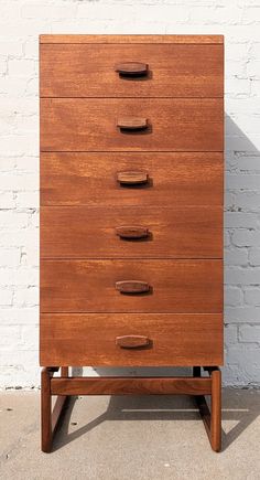 a wooden chest of drawers sitting in front of a white brick wall