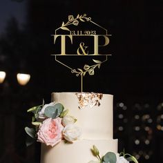 a wedding cake decorated with flowers and a monogrammed top is displayed on a table