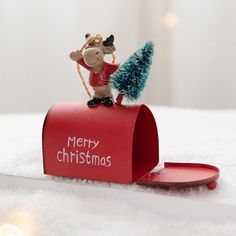 a small christmas tree sitting on top of a red mailbox with a reindeer figurine