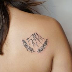 a woman with a tattoo on her shoulder has a mountain behind her back and leaves in the foreground