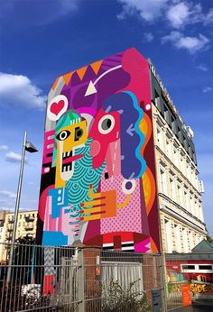 a large colorful building with people painted on it's side and fenced in area