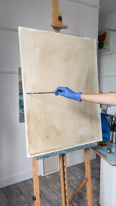 a person in blue gloves painting on an easel