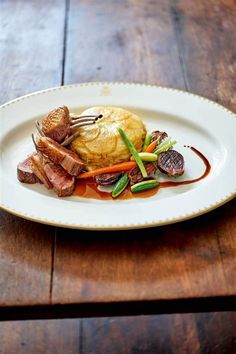 a white plate topped with meat and veggies on top of a wooden table