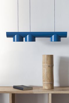 three blue lights hanging from the ceiling above a table with a book and vase on it