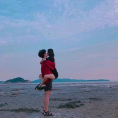 two people standing on the beach hugging each other