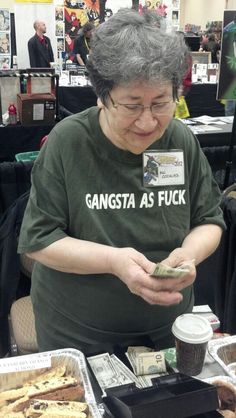 an older woman sitting at a table with food and money in front of her face