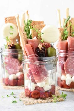 several mason jars filled with food and garnished with cheeses, olives, meat