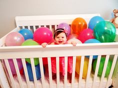 a baby in a crib surrounded by balloons