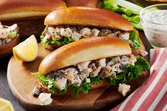 two sandwiches with meat, lettuce and sauce on wooden cutting board next to lemon wedges