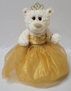 a white teddy bear wearing a yellow dress and a tiara on top of it