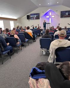 a group of people sitting in front of a church filled with blue chairs and microphones