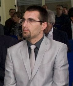 a man in a suit and tie sitting next to another man with glasses on his head