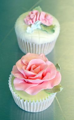 two cupcakes decorated with pink and green frosting on top of a table