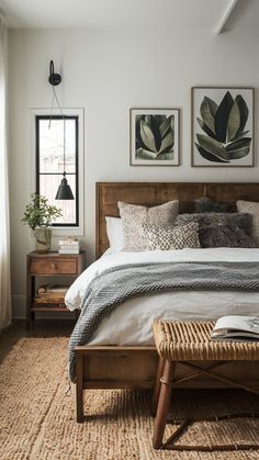 a bedroom with white walls and wooden bed frame, wicker footstool, two framed pictures on the wall