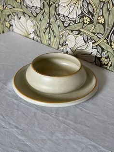 two white bowls sitting on top of a table next to a wallpapered wall