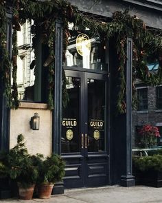 the front entrance to a restaurant with potted plants on the sidewalk and lights hanging from the windows