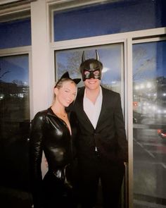 a man and woman dressed up as batman and catwoman pose for a photo in front of a window