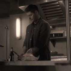 a man standing in a kitchen preparing food on top of a counter next to a bottle