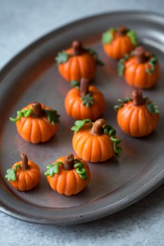 small pumpkins are arranged on a metal plate with leaves and sprigs in the middle