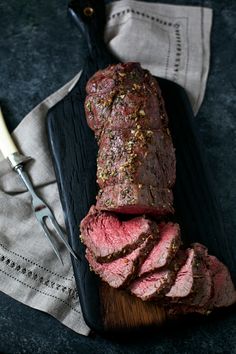 sliced steak on a black platter with a knife and napkin next to the meat