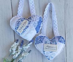 two blue and white heart shaped bags next to some flowers on a wooden table with lace