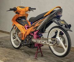 an orange and black motorcycle parked on top of a cement floor next to a wall