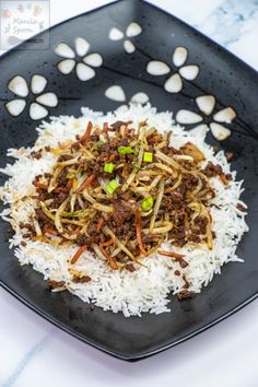 a black plate filled with rice and meat on top of a white tablecloth covered table