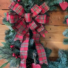 a christmas wreath with red and green plaid bow hanging on a wooden wall next to pine cones