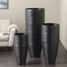 three black vases sitting next to each other on a wooden floor in front of a white couch