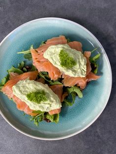 two pieces of salmon on top of lettuce in a blue plate with green sauce