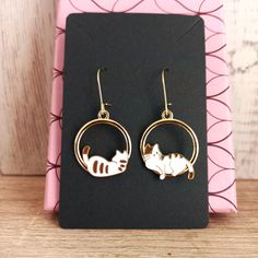 Cute golden hoop earrings with mismatched cats. One cat rests facing forward and the other one on its back.  Lovely valentines day gift for cat lovers Hypoallergenic stainless steel hooks. Enameled alloy metal rings with cats.  Hoops diameter is 2.2cms  Total drop length is 4.5cms  Weight: 2.6g These earrings are carefully shipped in a cardboard box to guarantee you will receive them in perfect conditions. Please specify if you want them as a gift when you are ordering. No additional cost Cardboardbox is handmade with recycled and sustainable material. #hoopearrings #cathoopearrings #carearrings #catlover #originalgift #originalhoops #originalearrings #catjewelry #cataccesories #mismatchedcatearrings #mismatchedearrings #valentinesday #giftforvalentinesday #loversday #friendshippresent #fr Gold Metal Cat Design Earrings, Gold Metal Earrings With Cat Design, Metal Jewelry With Cat Design, Metal Cat Design Round Jewelry, Gold Cat Design Earrings For Gifts, Cat Design Metal Drop Earrings, Cute Nickel-free Metal Hoop Earrings, Gold Cat Ears Jewelry Gift, Gold Cat Ears Jewelry As Gift