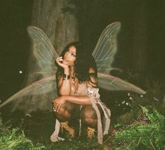 a fairy sitting on the ground next to a tree