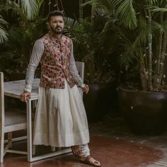 a man standing next to a table in front of potted plants and greenery