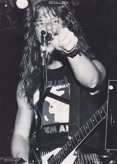 a man with long hair holding a guitar in his right hand and singing into a microphone