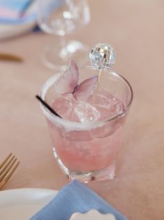 a pink drink in a glass with a butterfly on the top and some silverware next to it