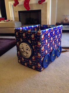 a christmas present box sitting on the floor in front of a fireplace