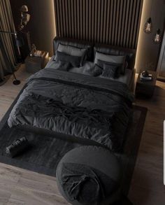 a large bed with black sheets and pillows in a dark colored room, surrounded by wooden flooring