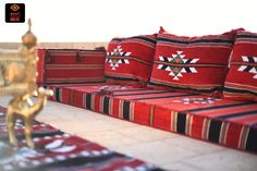 a red couch sitting on top of a tiled floor next to pillows and rugs