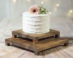 a white cake sitting on top of wooden pallets with a pink flower in the middle