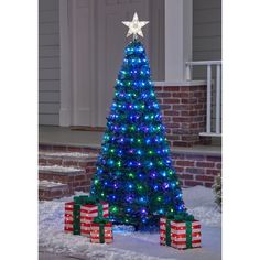 a blue christmas tree with lights and presents under it in the middle of some snow