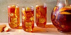 several glasses and pitchers filled with liquid next to sliced oranges on a wooden table