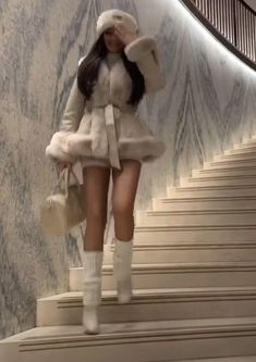 a woman in white is walking down the stairs with her hand on her head and she's wearing a fur coat