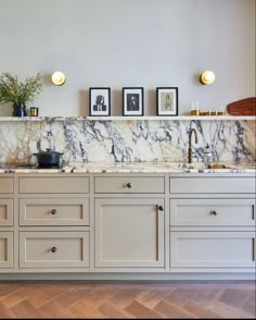 a kitchen with marble counter tops and white cabinets, framed pictures on the wall above it