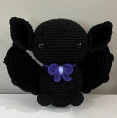 a crocheted black bat with purple flowers on it's chest and wings