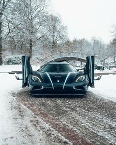 a black sports car with its doors open on a snowy road in front of some trees