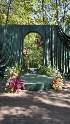 an outdoor ceremony with green drapes and flowers on the ground in front of it