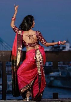 a woman in a red and gold sari is standing by the water with her arms outstretched